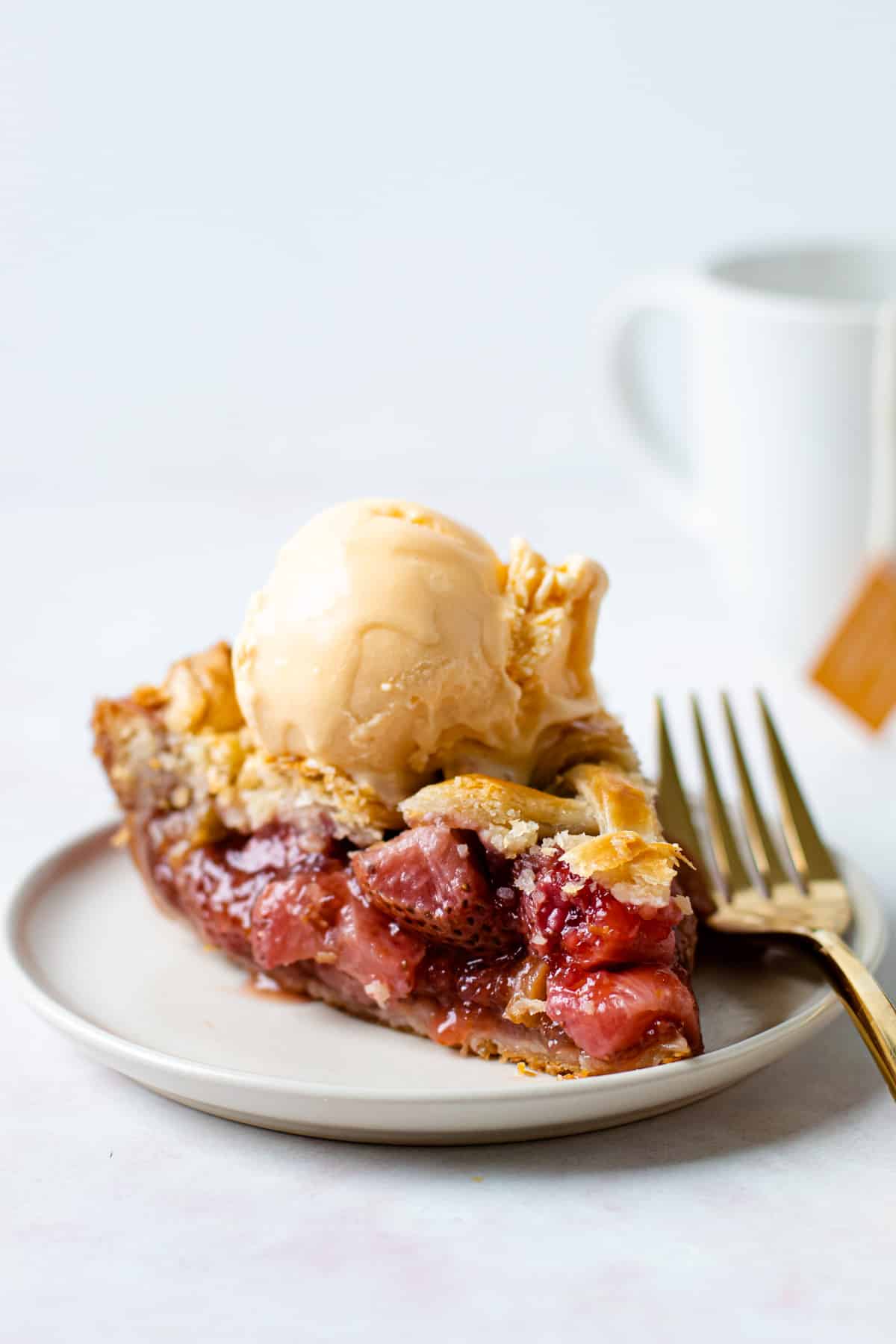 A slice of strawberry rhubarb pie with ice cream on it on a place.