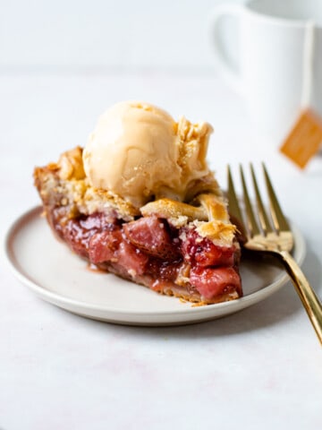 A slice of strawberry rhubarb pie with ice cream on a plate.