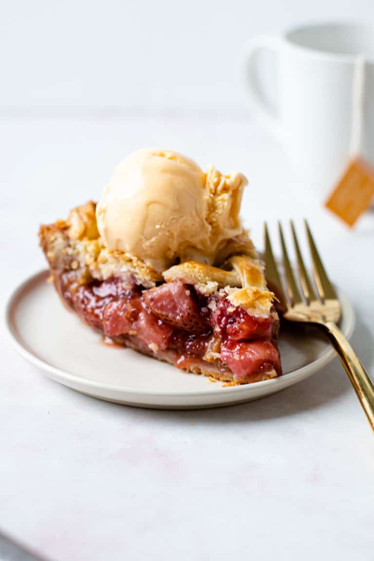 A slice of strawberry rhubarb pie with ice cream on a plate.