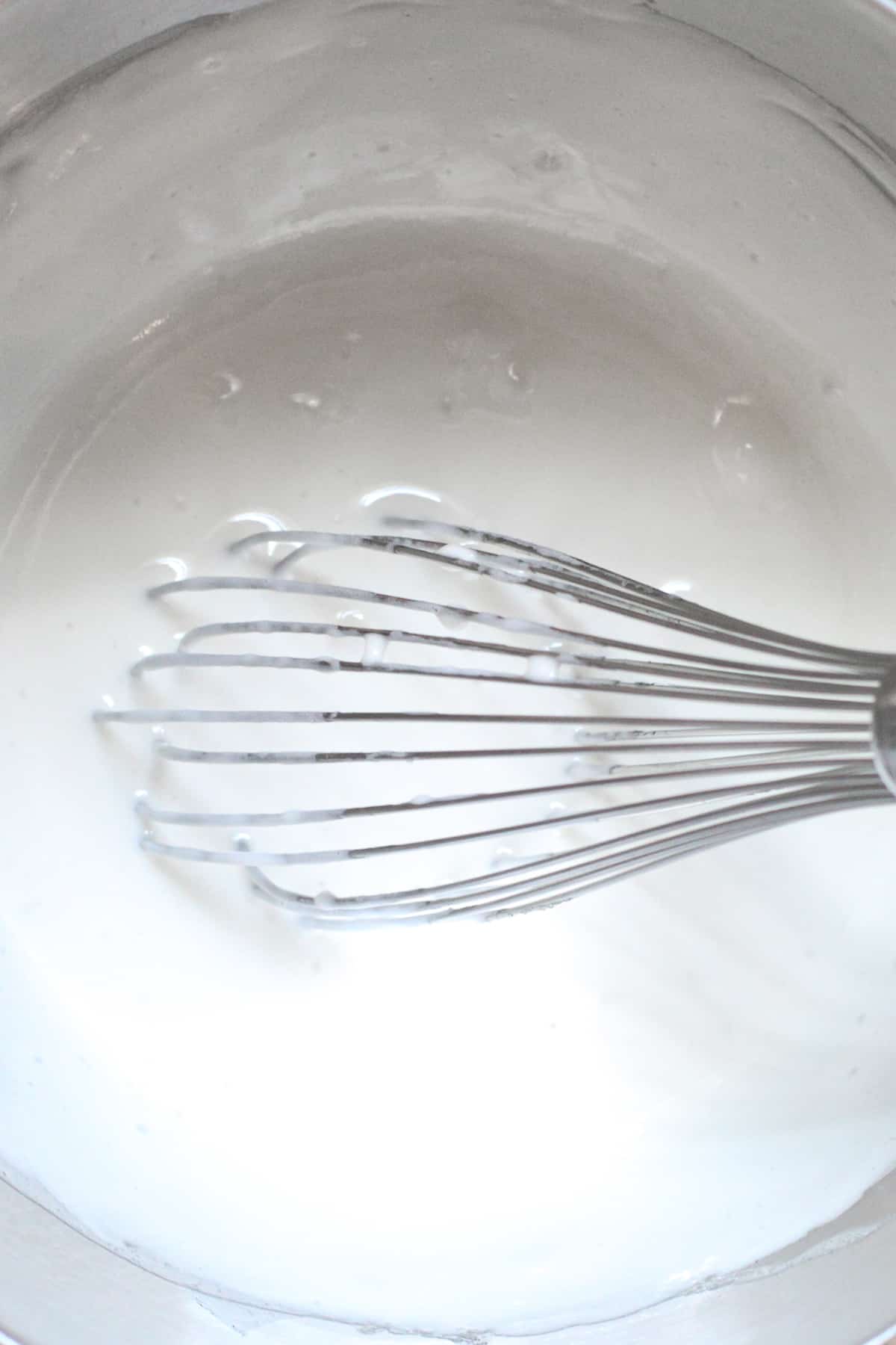 Egg whites and sugar are heated and whisked on a stove.