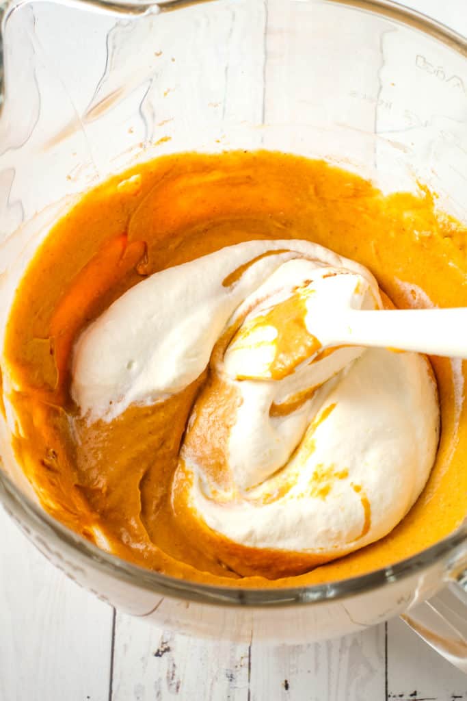 Folding ingredients in a bowl for a no bake pumpkin pie filling.