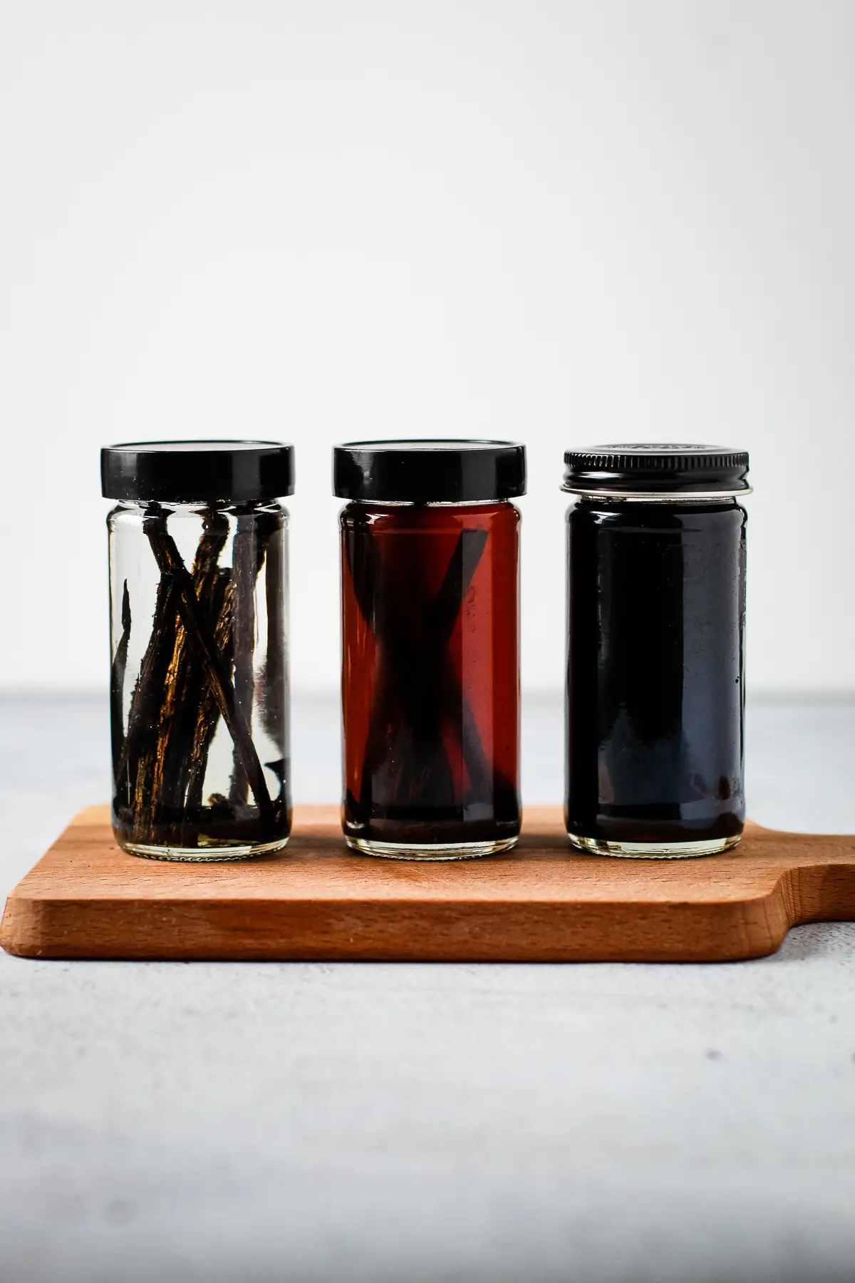 Three jars of homemade vanilla extract with different levels of darkness.