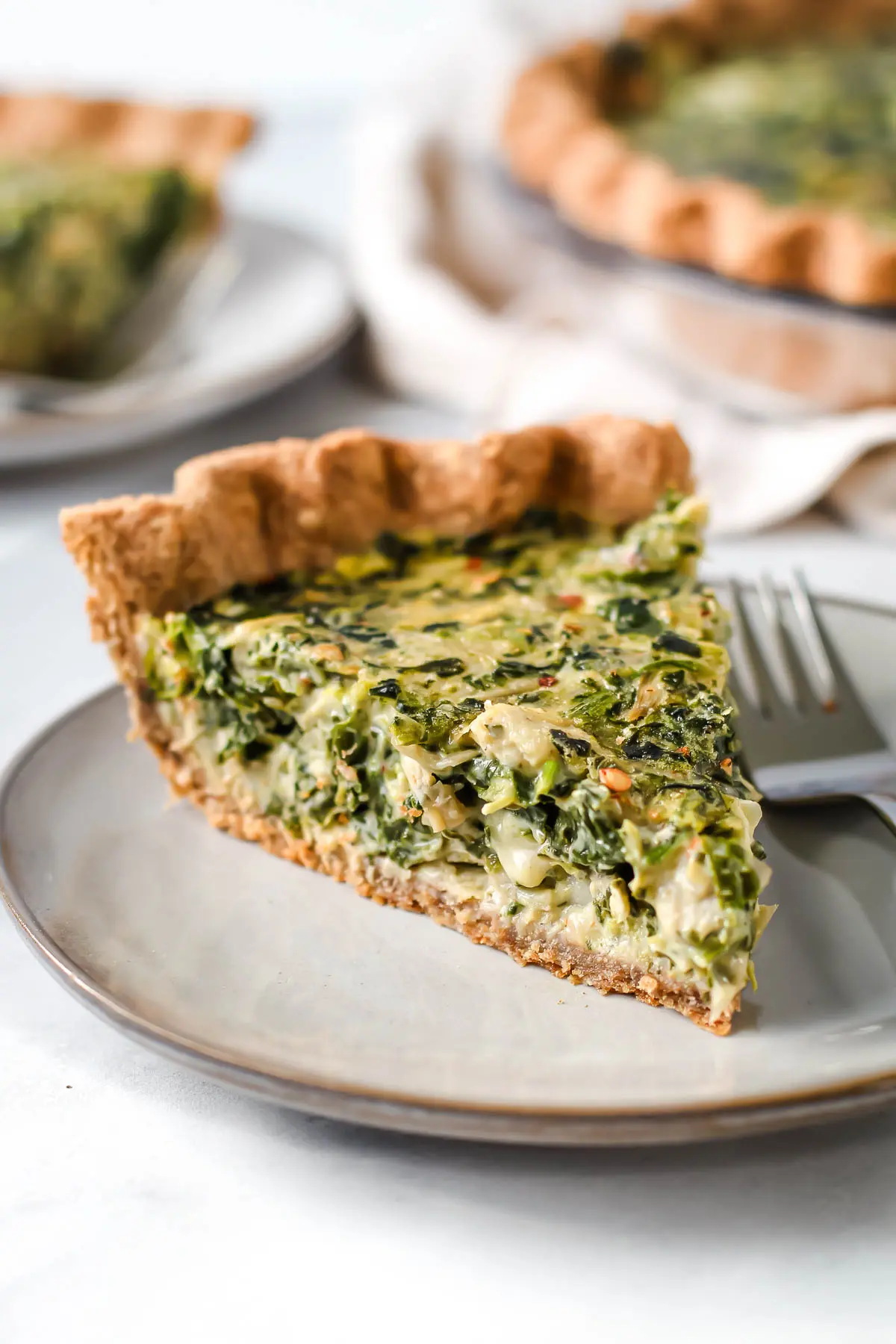 Slice of spinach artichoke quiche on a plate.