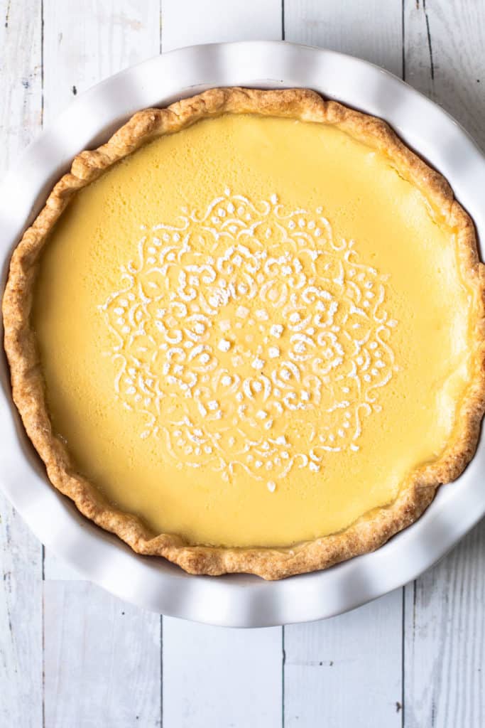 A baked lemon custard pie with a decorative dusting of powdered sugar on it.