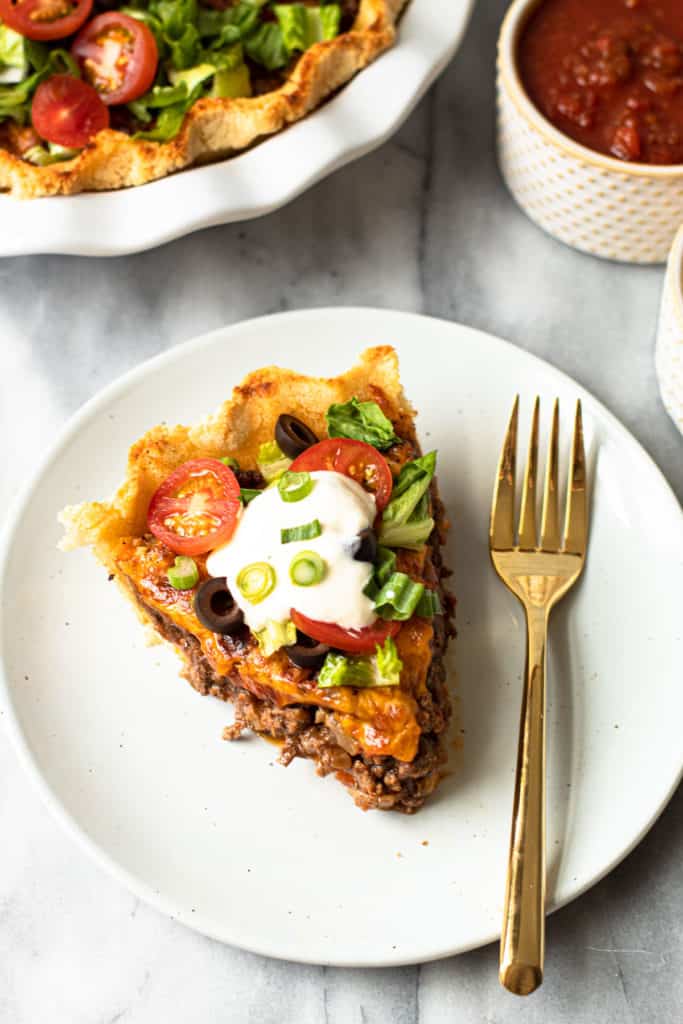 A slice of beef taco pie with toppings and sour cream.