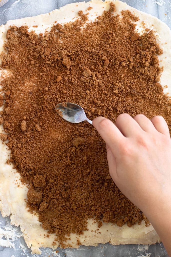 Spreading cinnamon and brown sugar on pie dough.