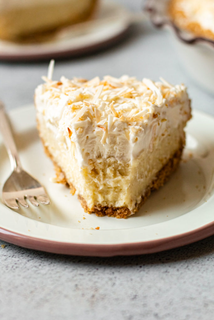 A slice of coconut cream pie on a plate with a bite taken out of it.