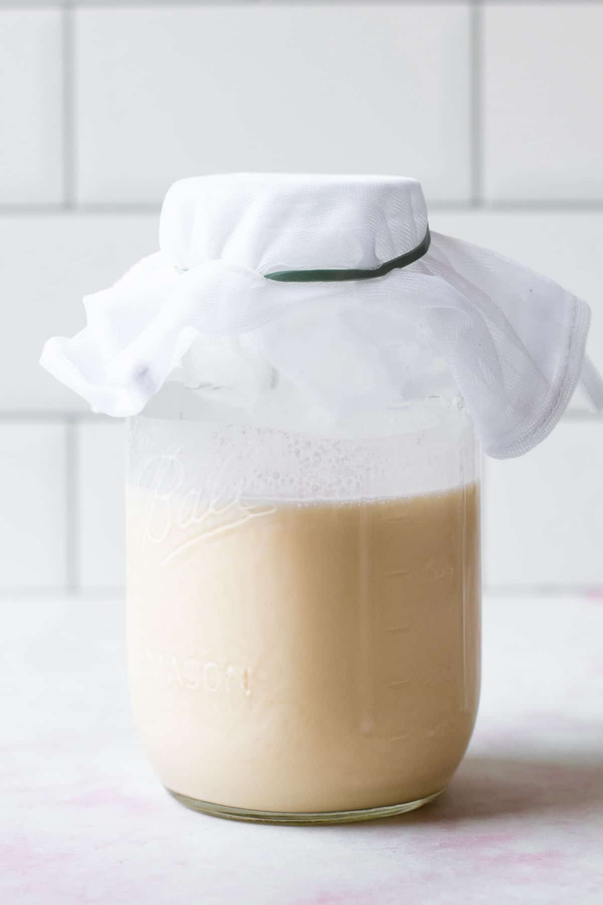 A jar of homemade creme fraiche with cheesecloth on it.