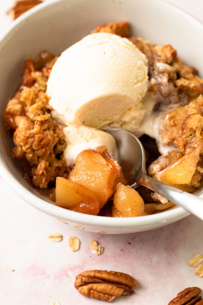 A bowl of healthy apple crisp with a scoop of vanilla ice cream on it.