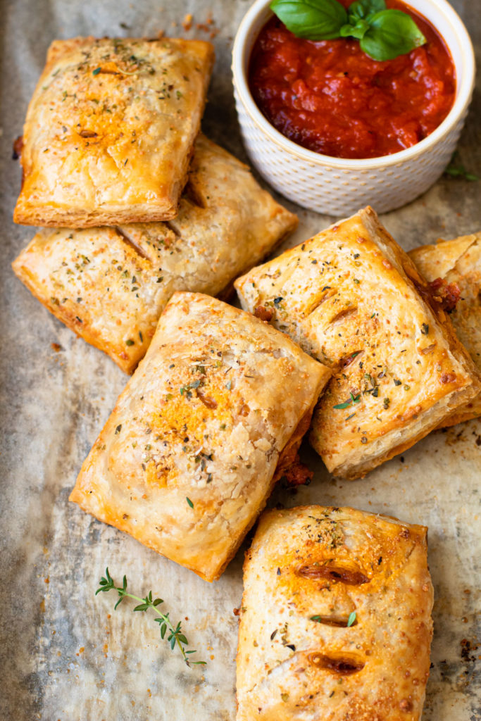 Pizza hand pies on a baking sheet with marinara dipping sauce.