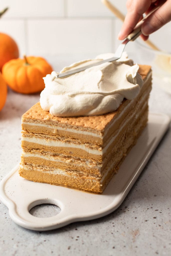 A no bake pumpkin layer cake being covered in whipped cream.