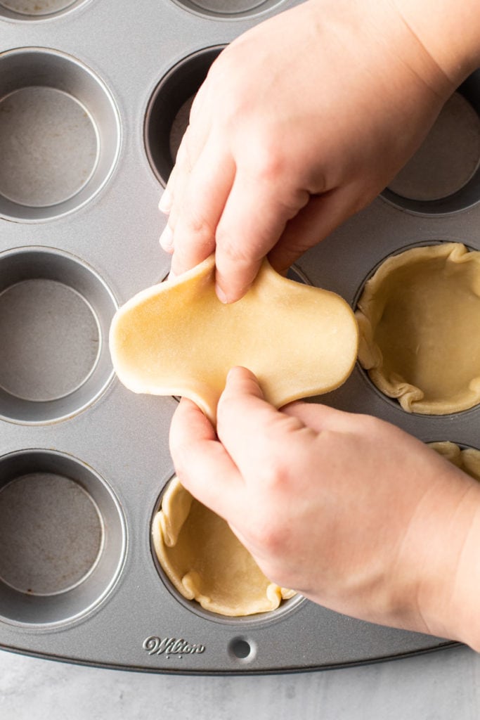 Placing dough into a muffin tin for mini pies.