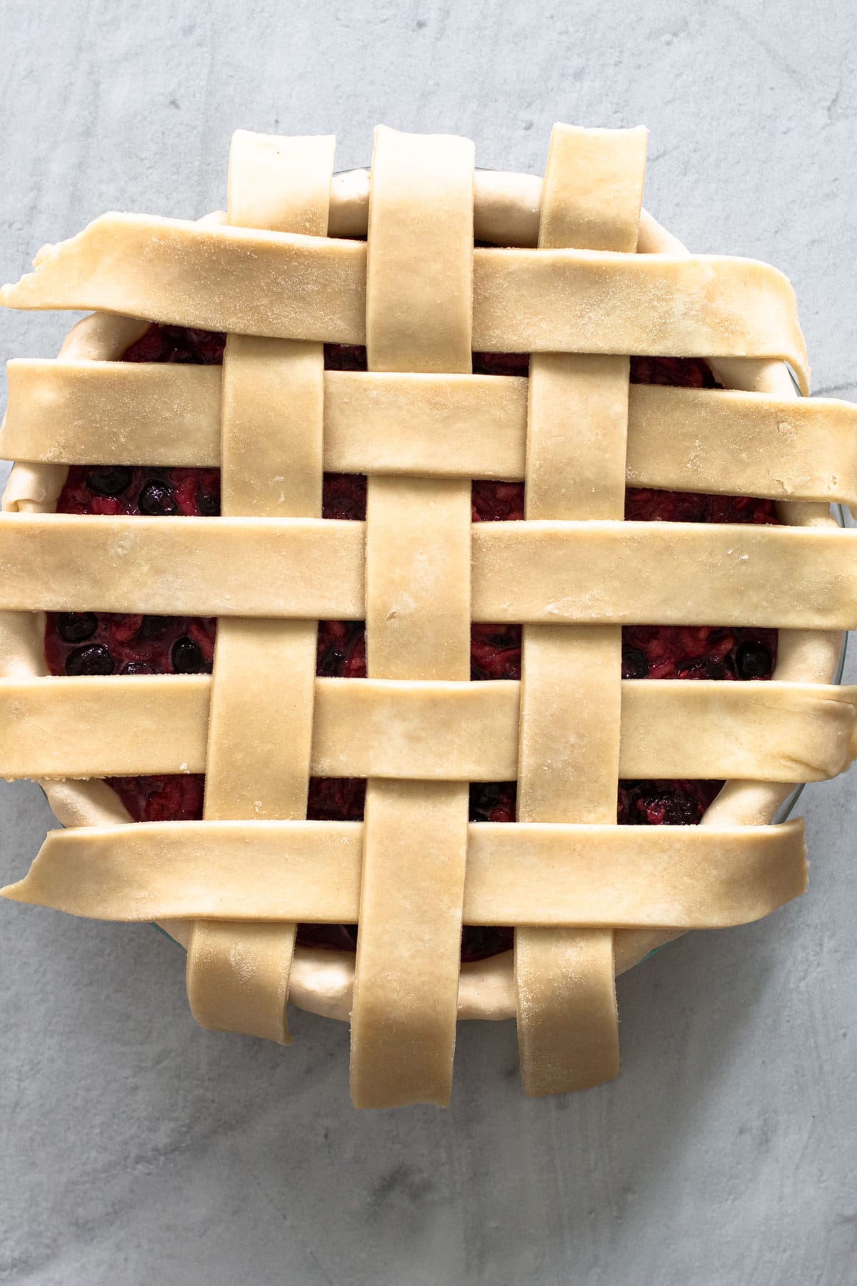 An unbaked pie being topped with a lattice crust.