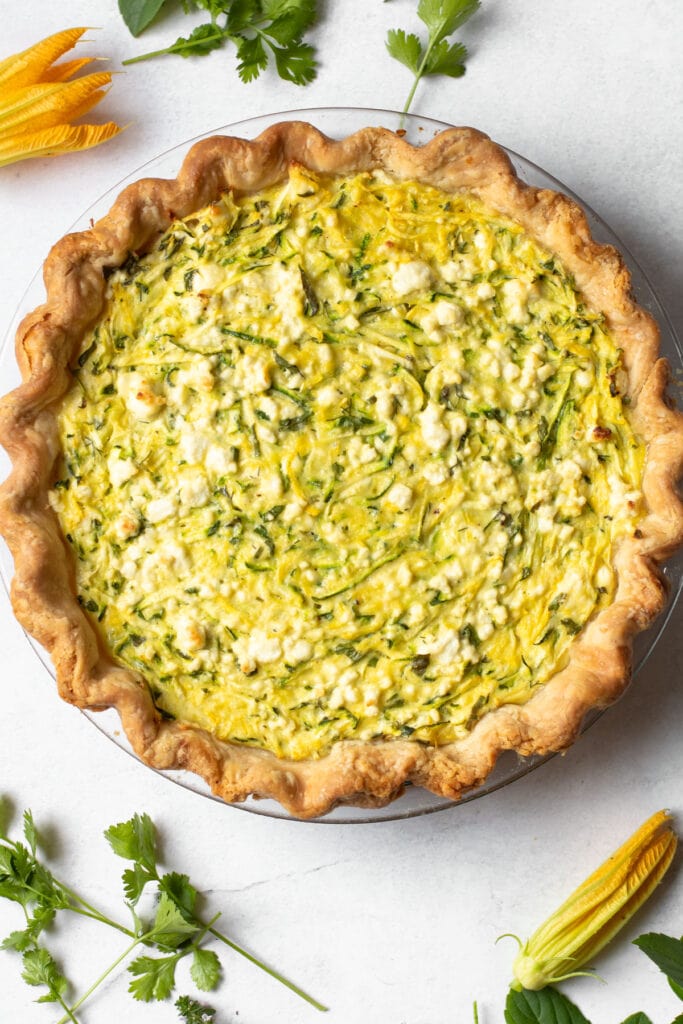 Zucchini Pie with goat cheese surrounded by fresh herbs