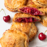 A pile of cherry hand pies with one broken open to reveal the cherry filling.