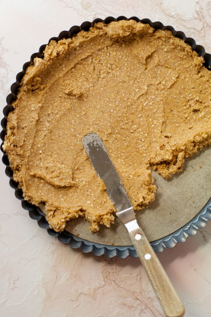Oat shortbread crust being smoothed over in a tart tin.