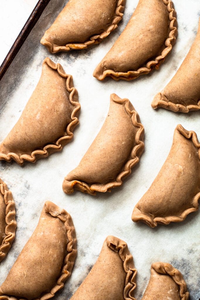 Unbaked pumpkin pasties on a sheet tray.