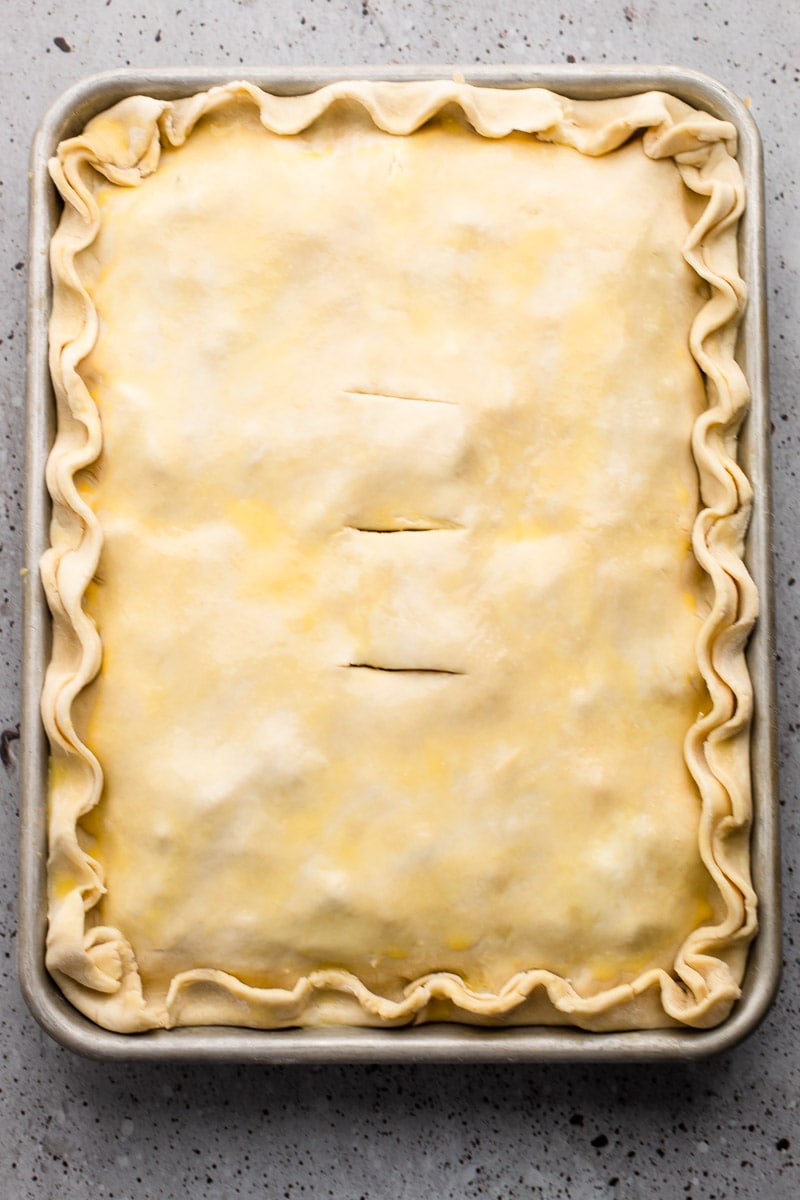 A fulled assembled breakfast slab pie with an egg wash before it's baked.