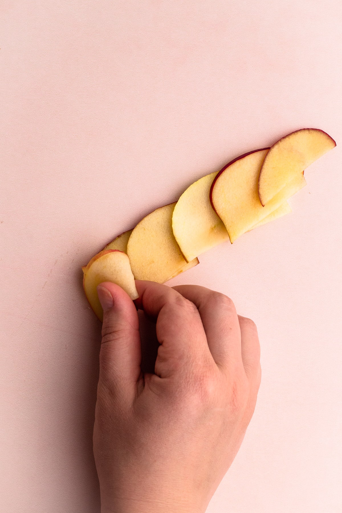 Rolling up apple slices on a work surface to make an apple rose.