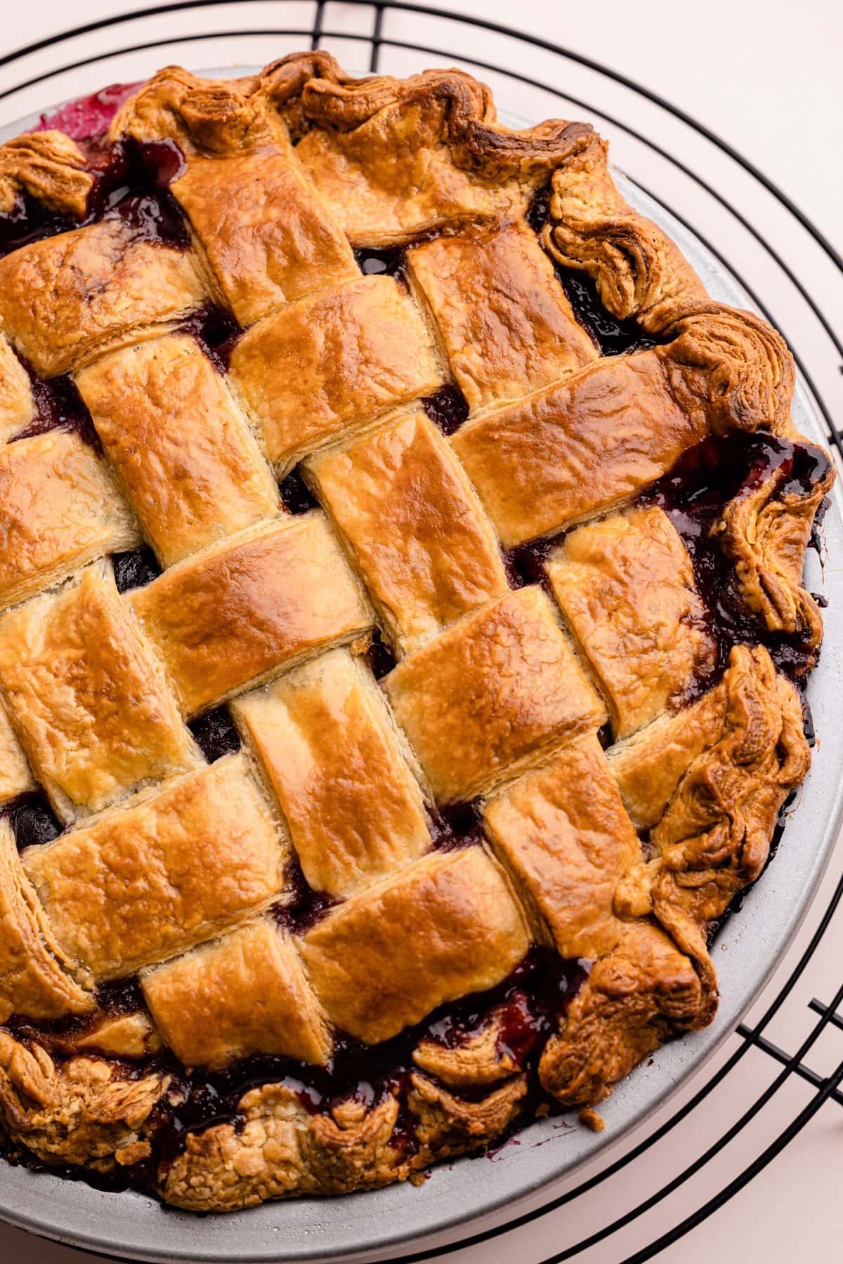 A golden and flaky sweet cherry pie on a cooling rack.