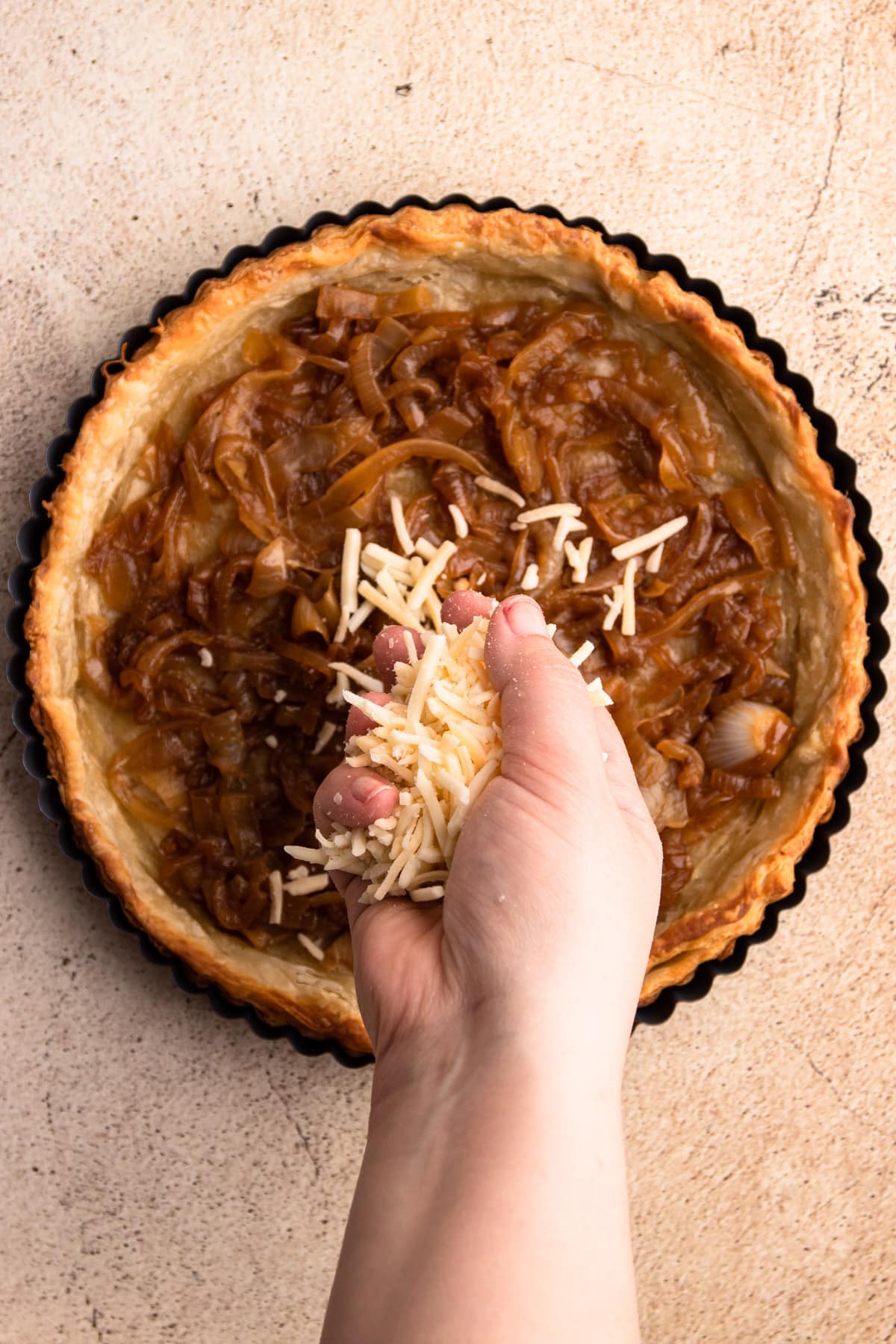 Putting cheese in a caramelized onion quiche.