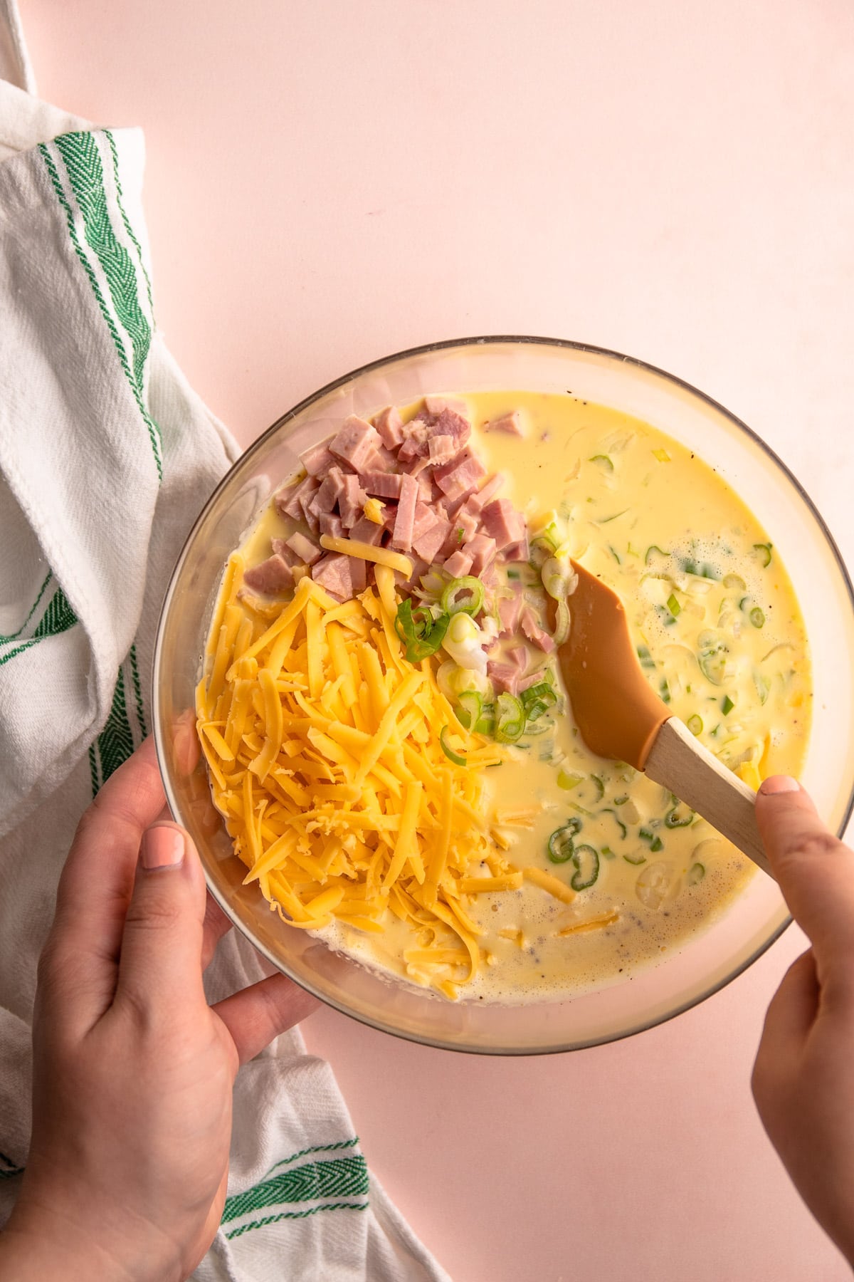 Adding ham and cheese quiche filling ingredients in a bowl.