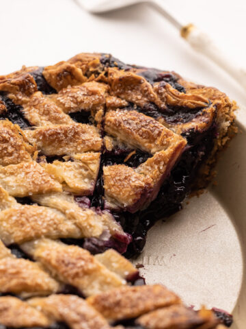 A slice of the best blueberry pie in a pie pan.