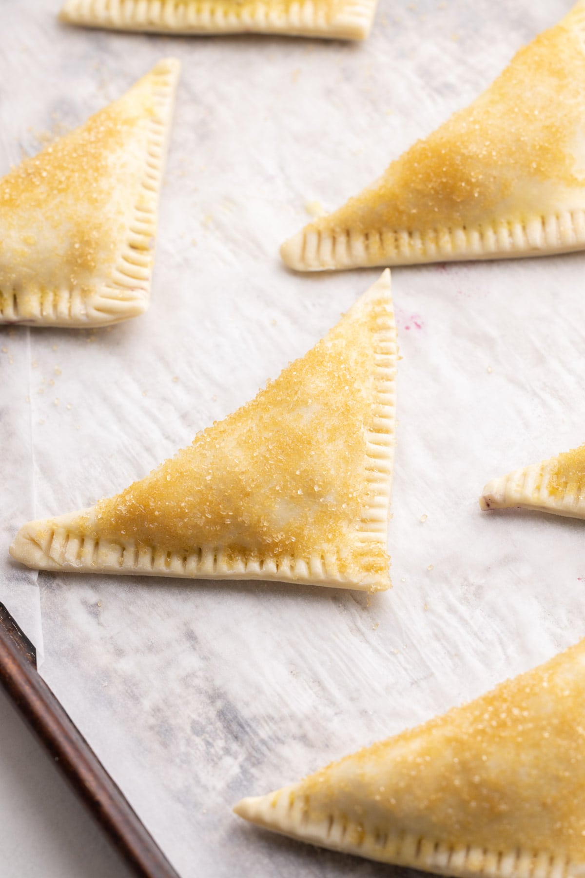 Blueberry turnovers unabaked with an egg wash and coarse sugar.