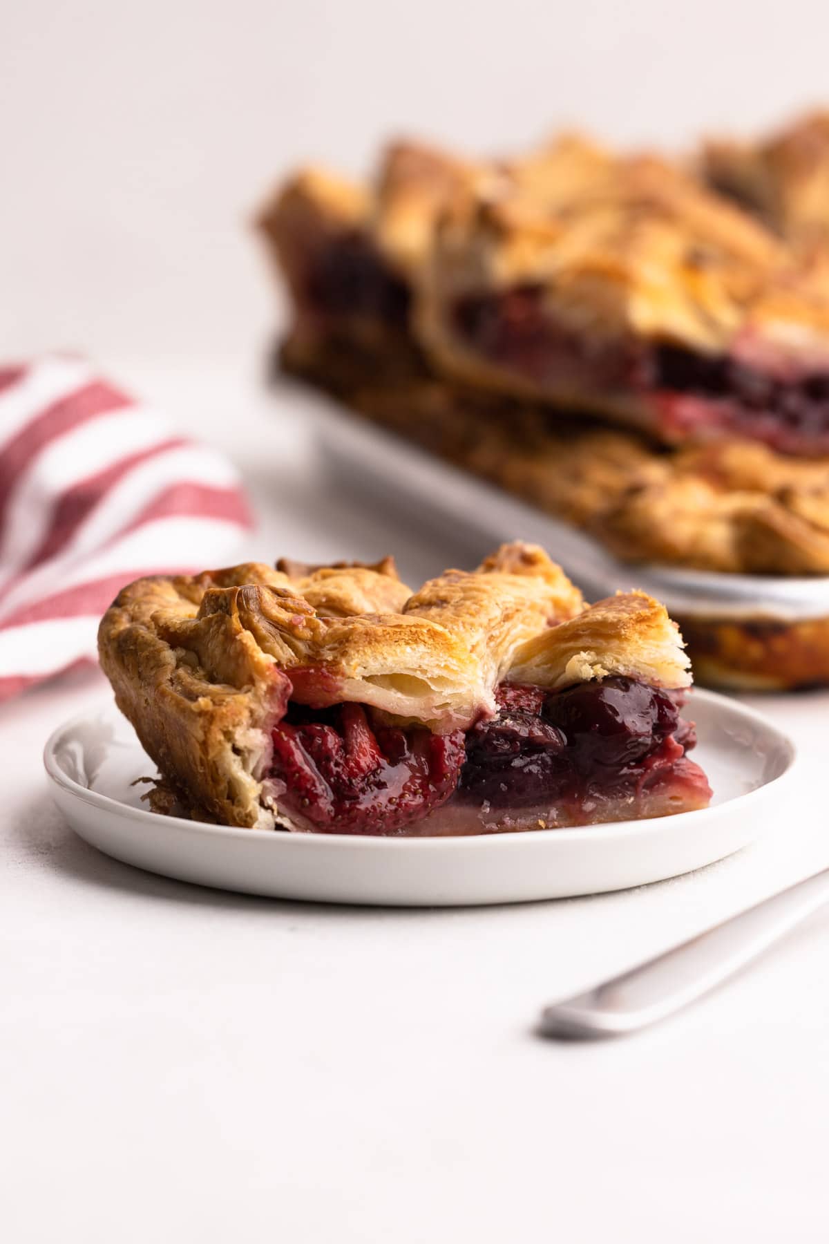 A slice of cherry strawberry slab pie on a plate next to a red napkin.