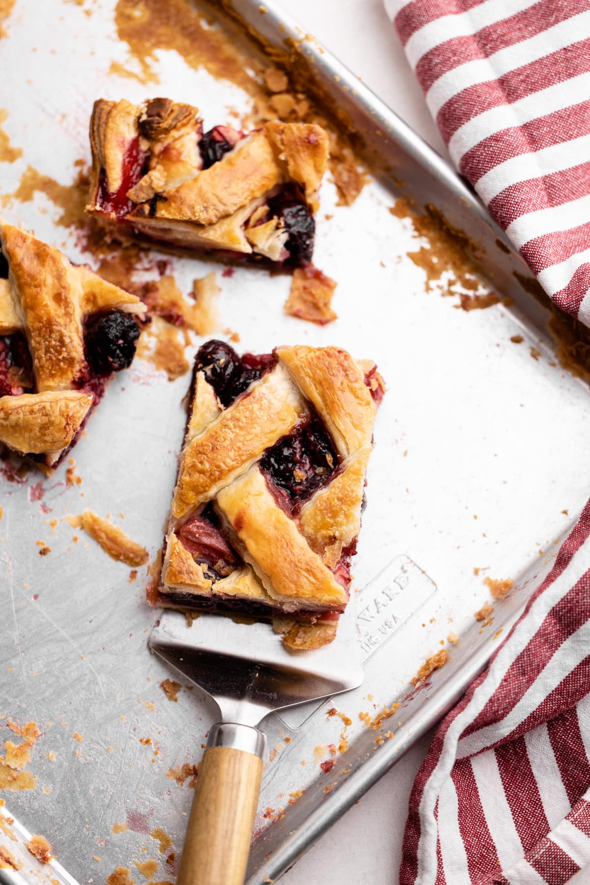 Slices of cherry strawberry slab pie on a sheet tray.