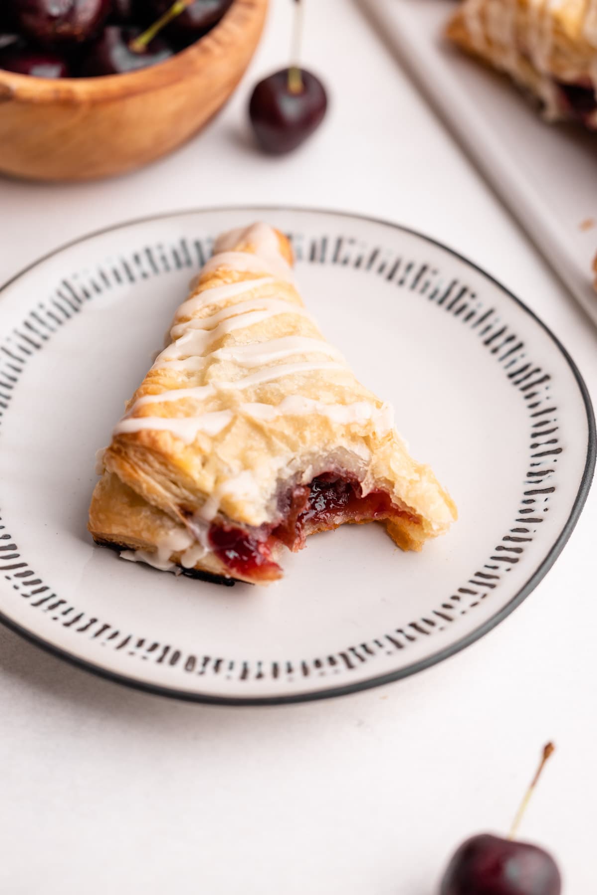 A cherry turnover on a plate with a bite taken from it.