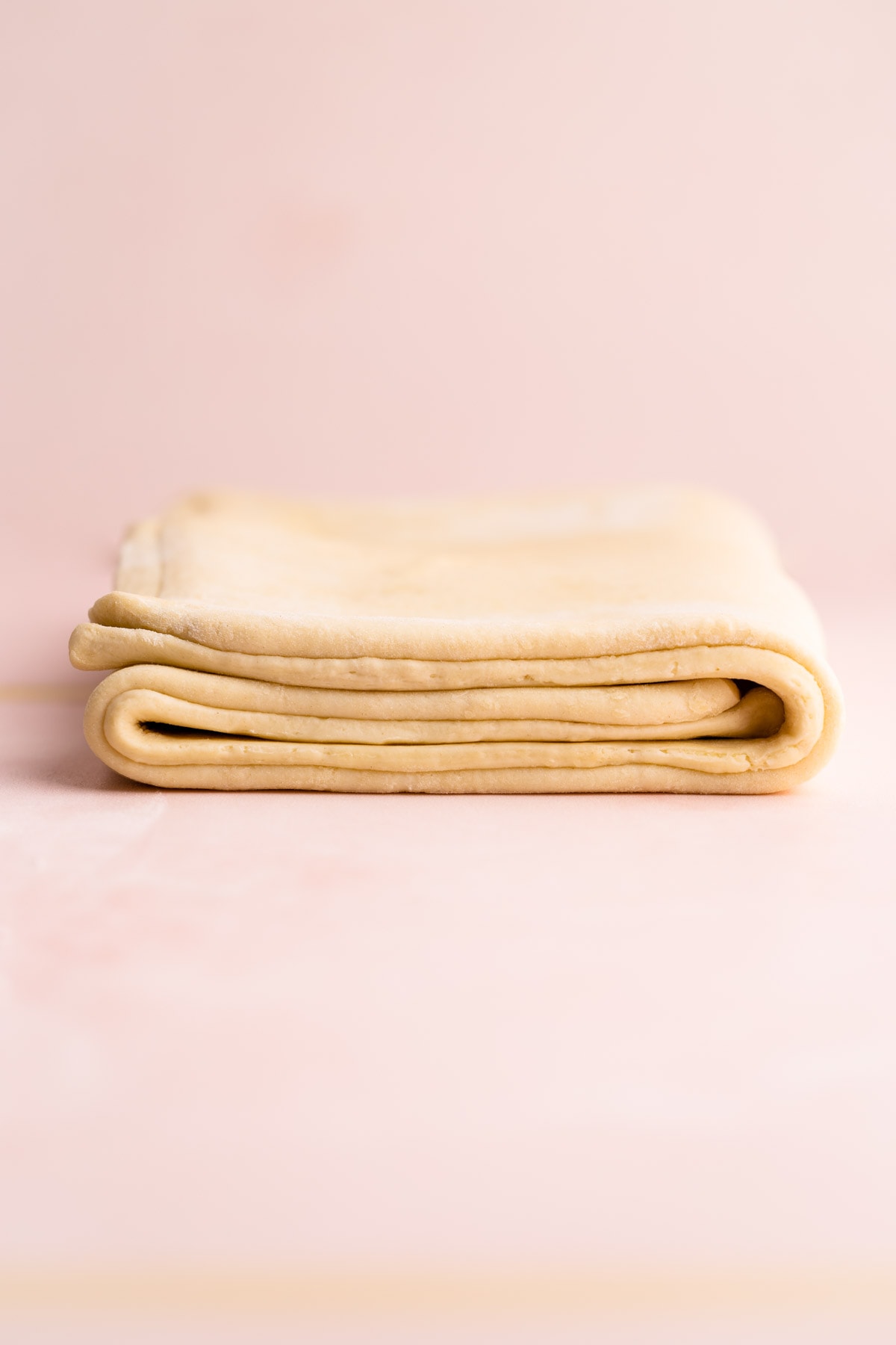 A layered puff pastry dough sitting on a pink surface.