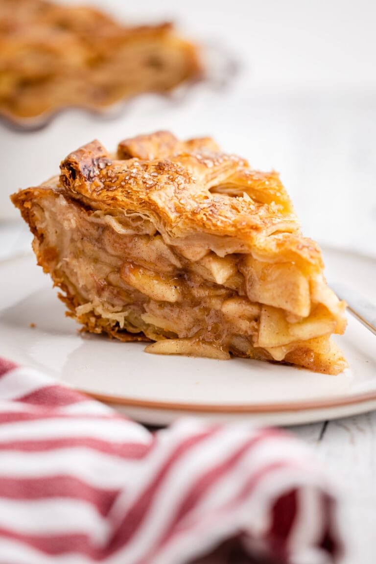 A slice of apple pie with a flaky pie crust on a plate.