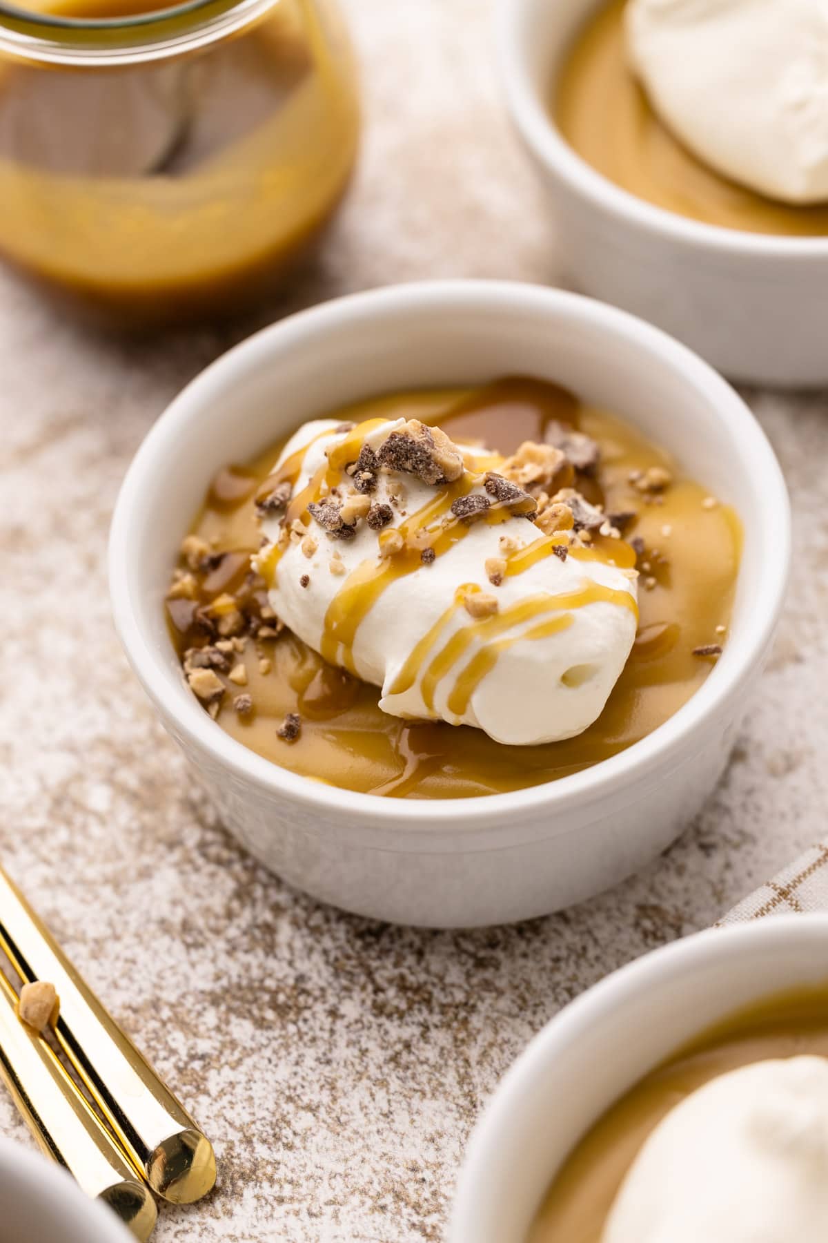 A small white bowl of homemade butterscotch pudding with whipped cream and chopped toffee.