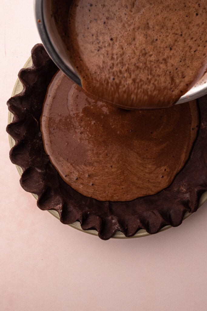 Pouring hot cocoa pie filling inside a chocolate crust.