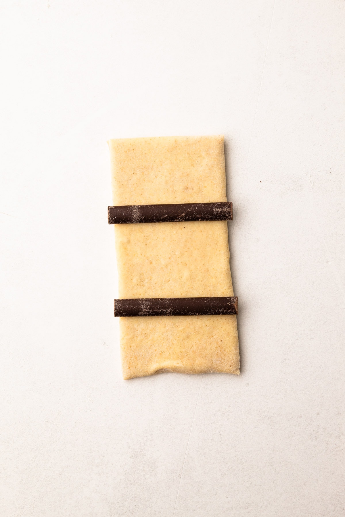 A sheet of croissant pastry with two sticks of chocolate on it.