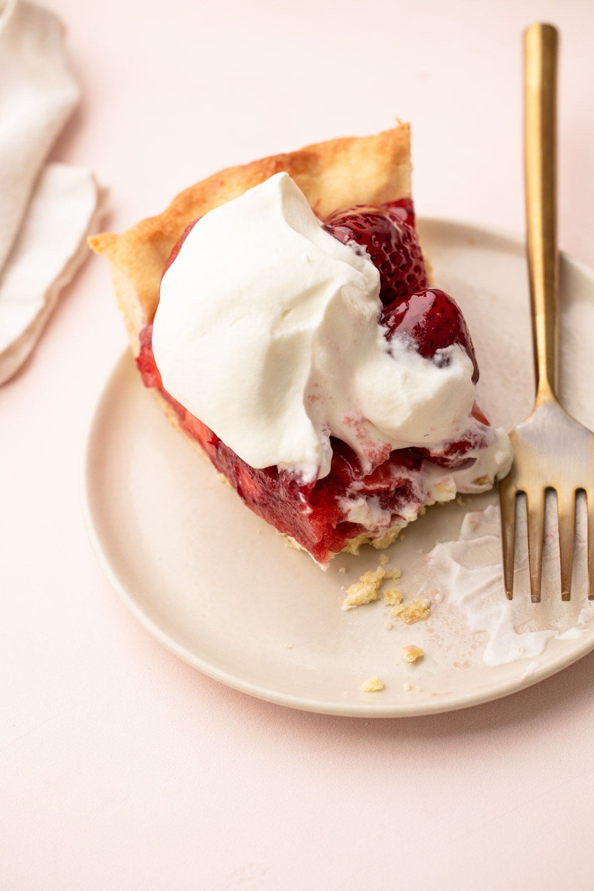 A messy and delicious fresh strawberry pie with whipped cream.