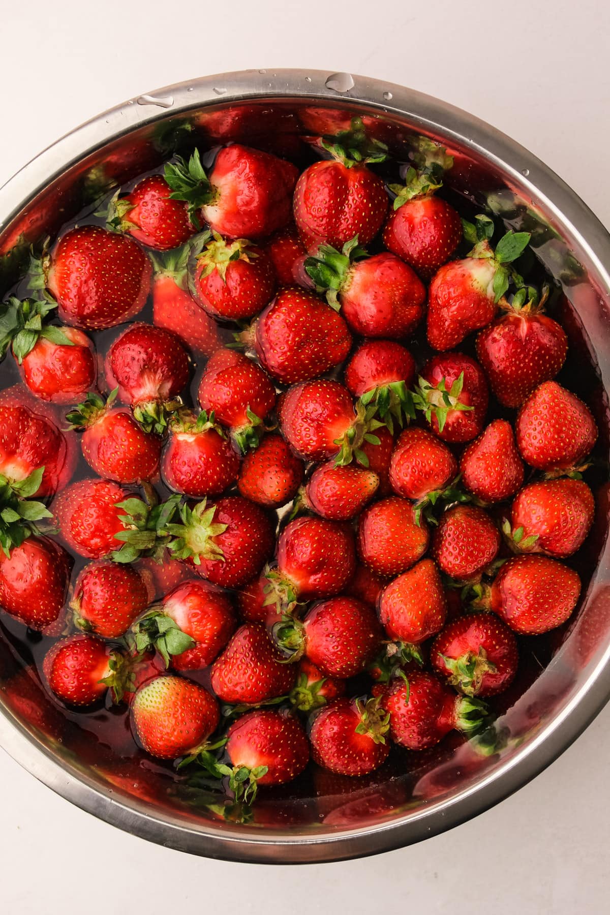 A bowl of strawberries getting cleaned.