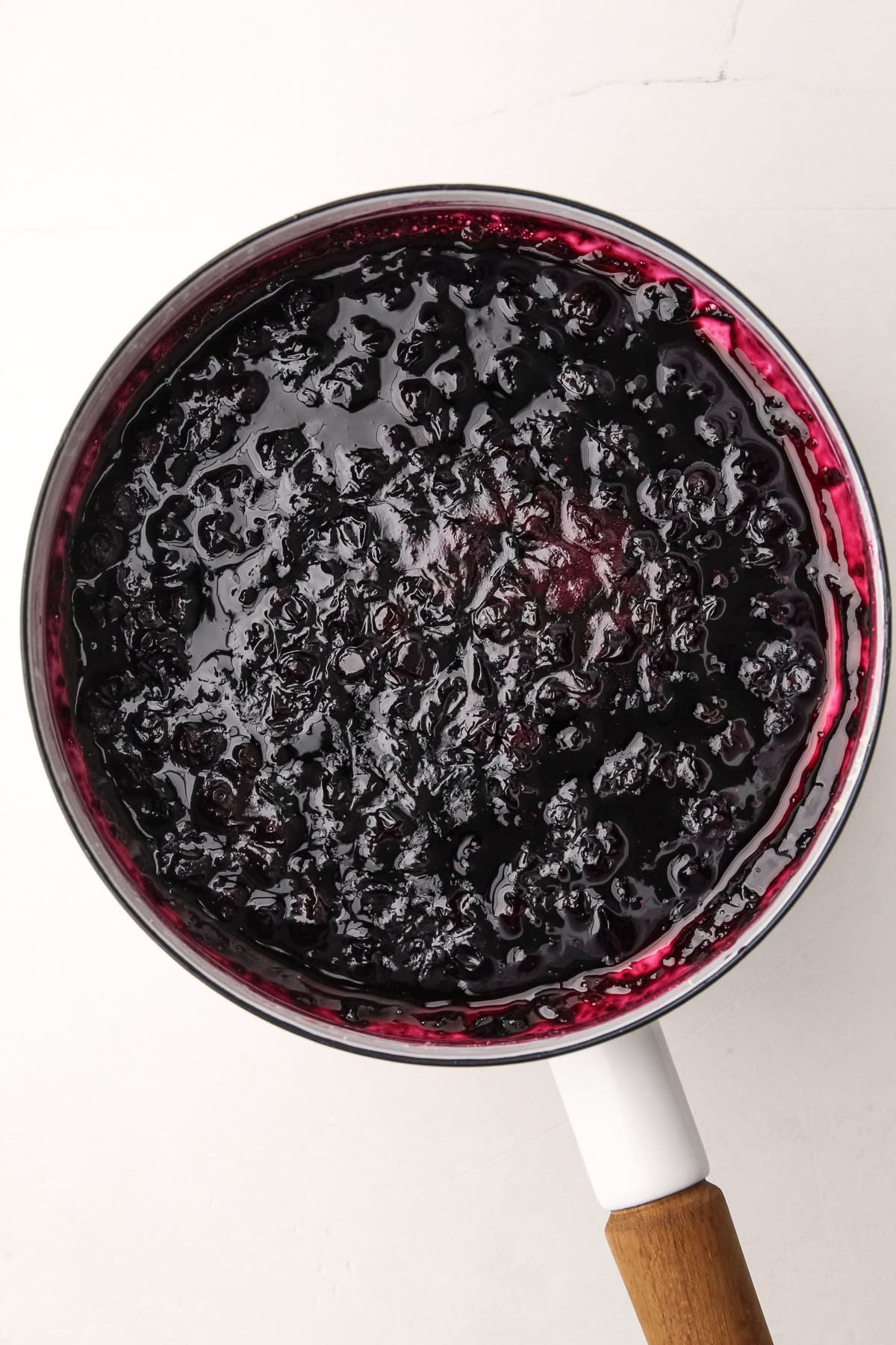 Cooked blueberries in a white pot.