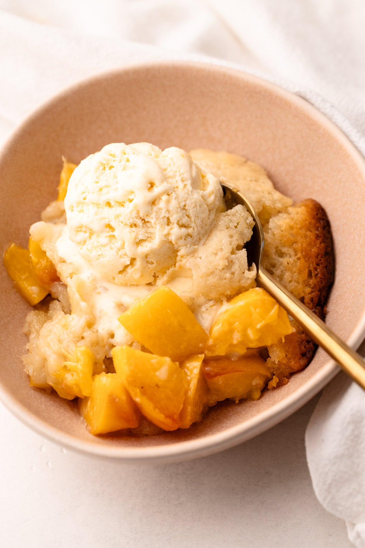 A scoop of peach ice cream on top of peach cobbler.