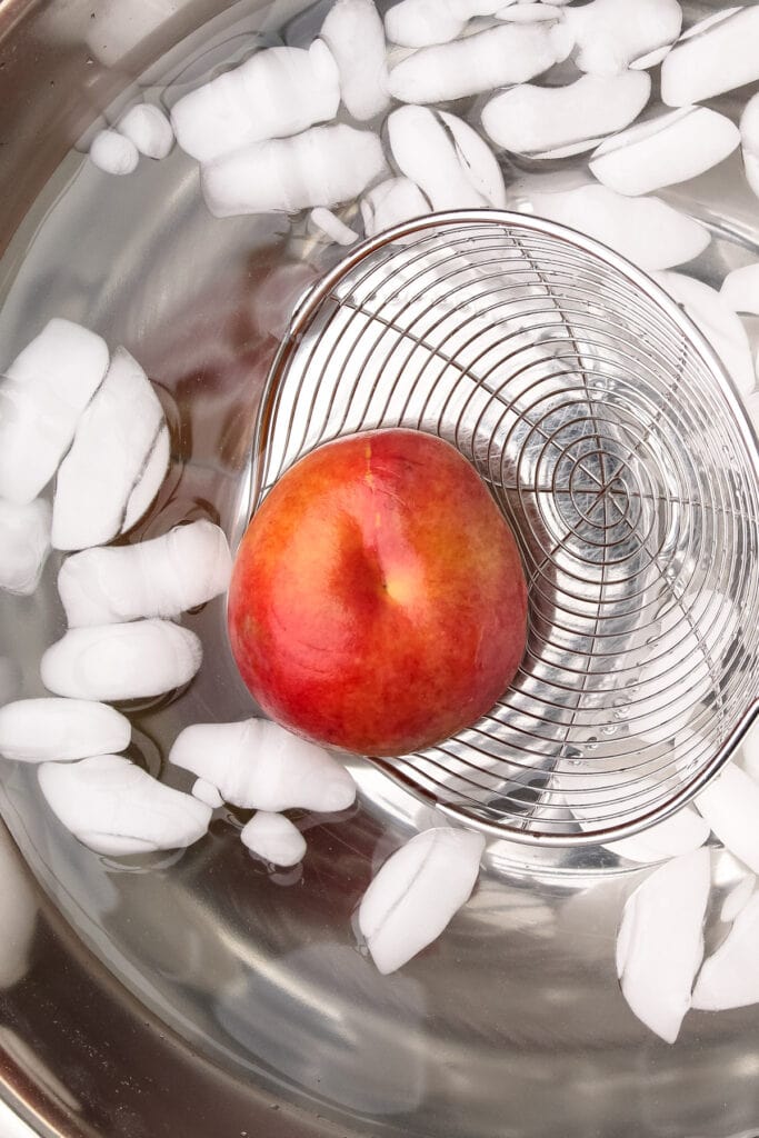 Placing a blanched peach in an ice bath.