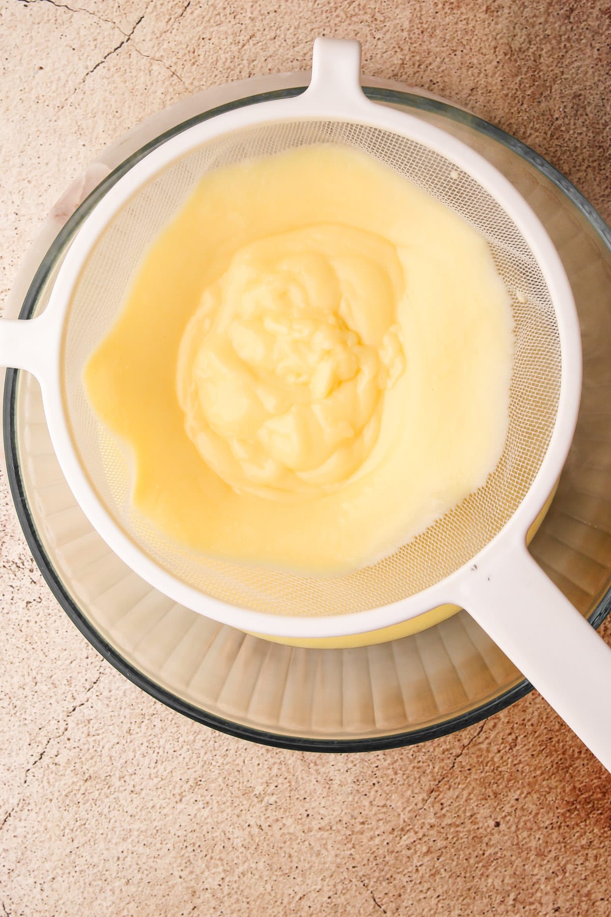 Straining cooked vanilla pudding into a glass bowl.