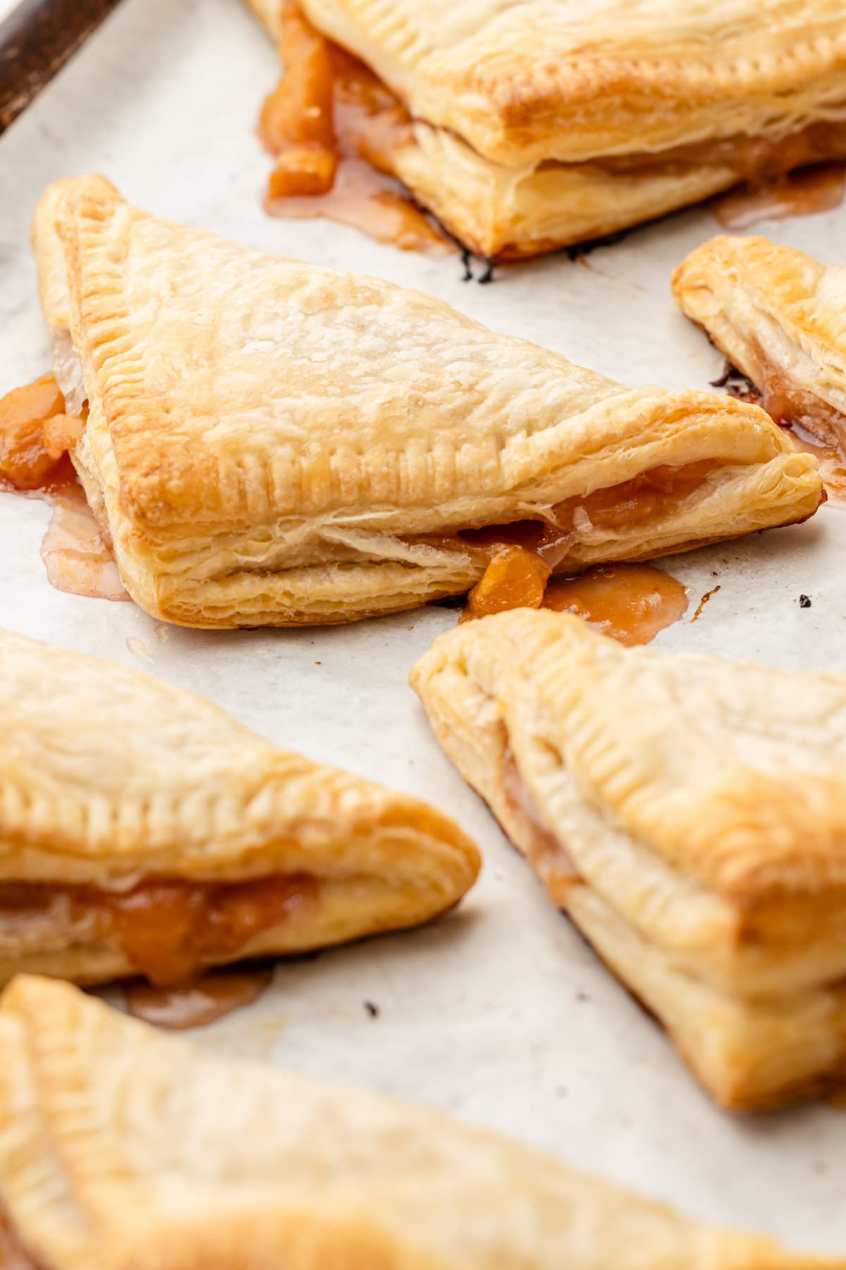 Six peach turnovers baked on a sheet tray.