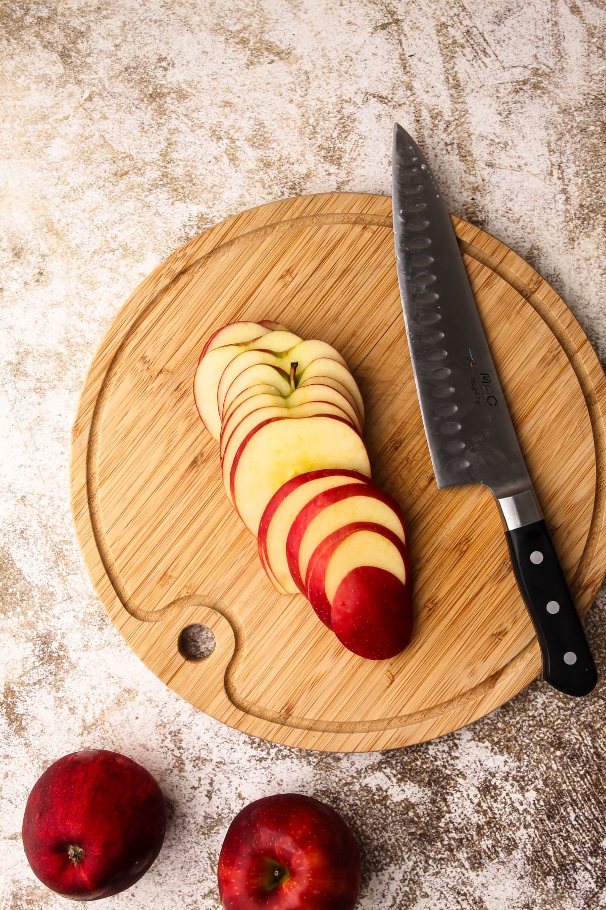 Apples cut into thin whole slices on a cutting board with a knife.