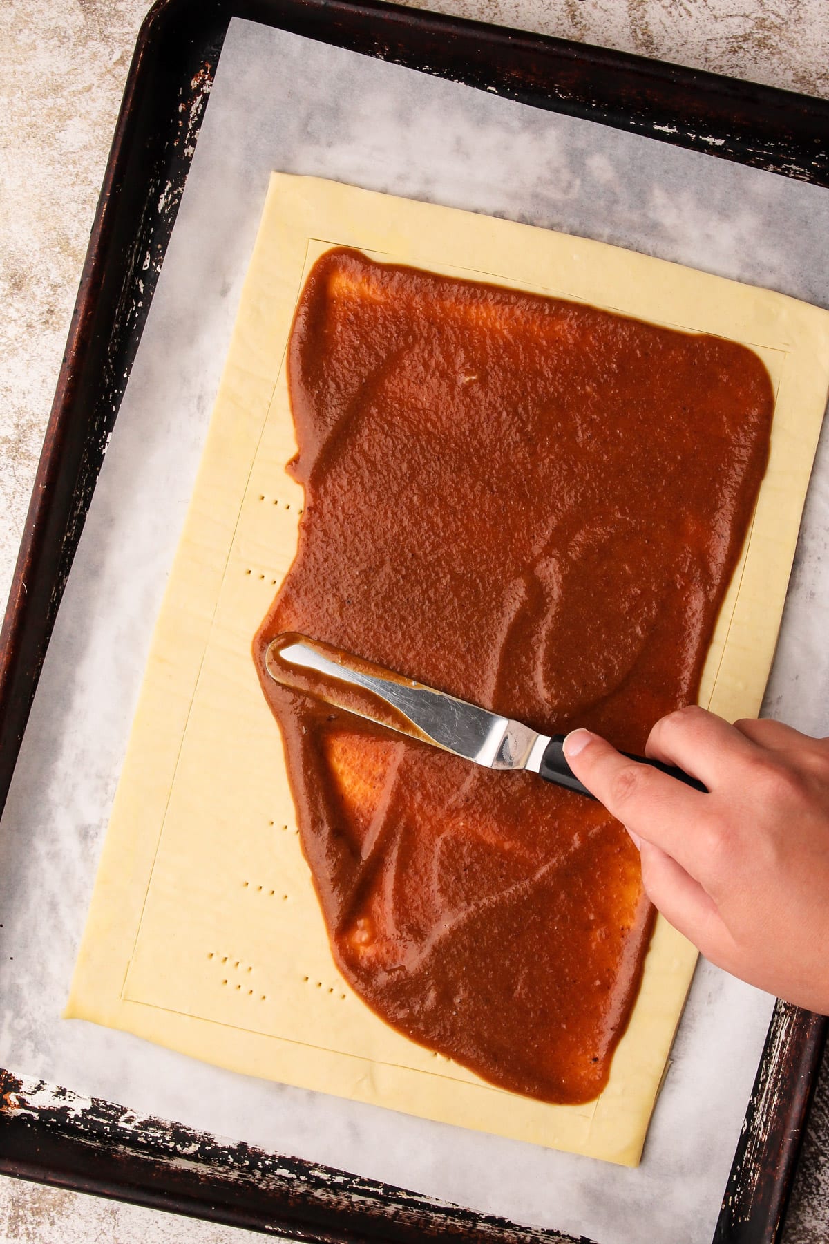 Spreading the apple filling on the puff pastry for an apple tart.