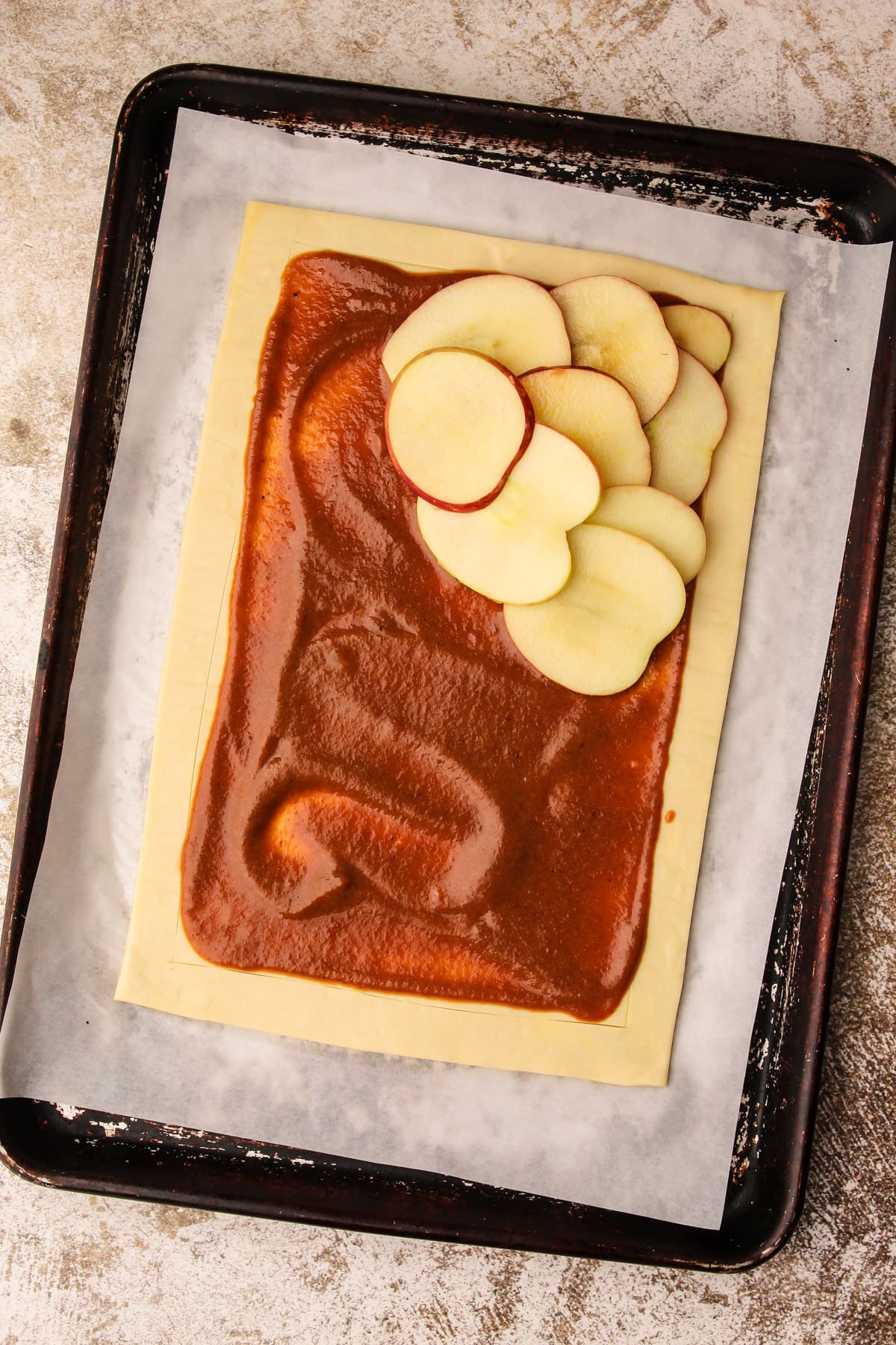 Apples half shingled on a piece of puff pastry with apple filling underneath unbaked.