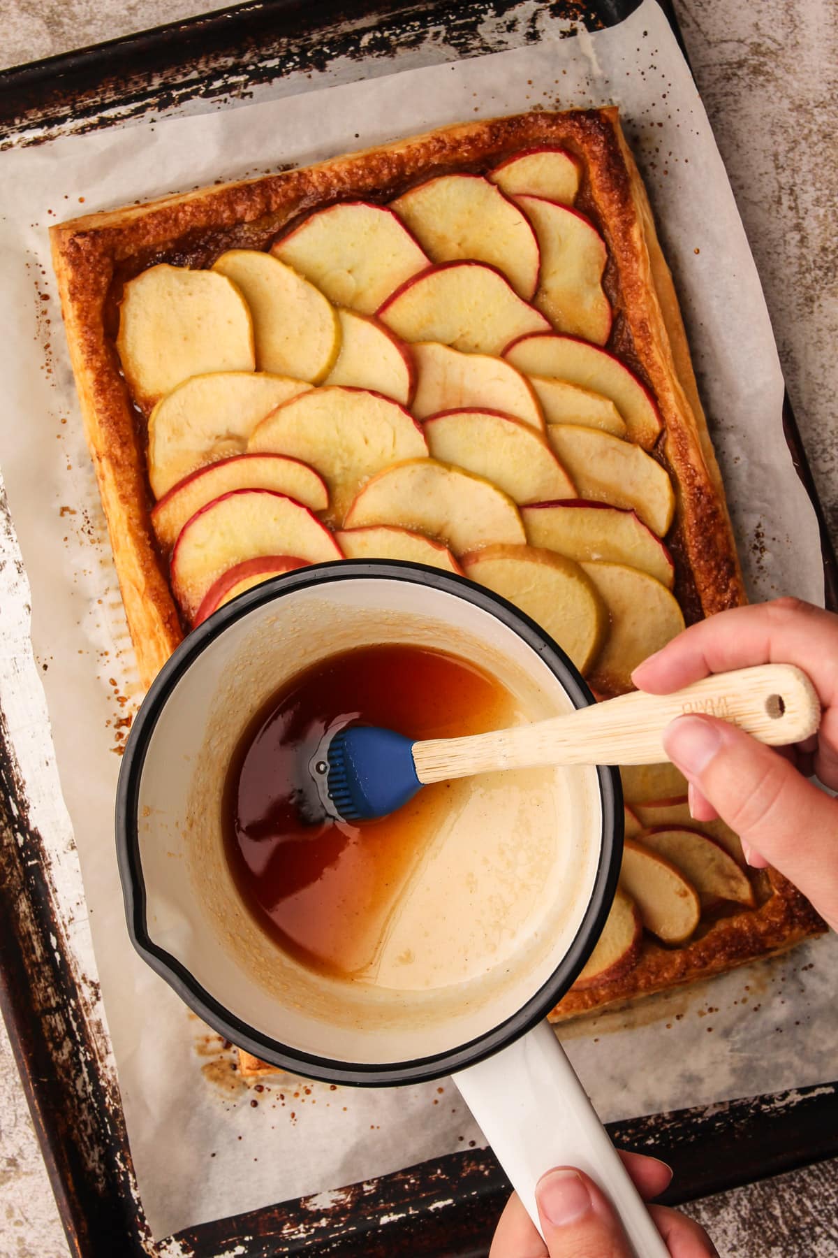 A silicone pastry brush inside of a pot with glaze before spreading on an apple tart.