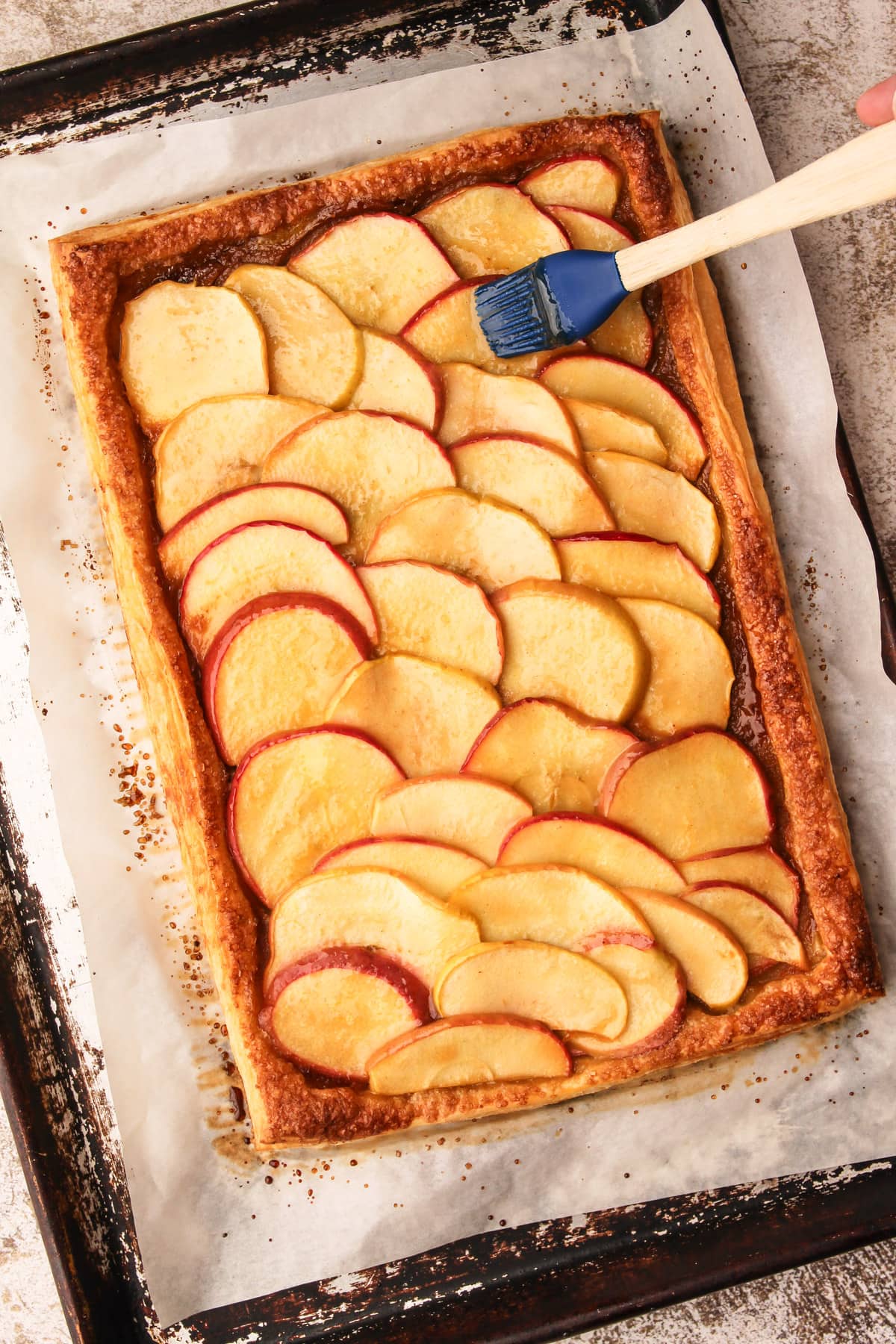 Spreading apple glaze on an apple tart on puff pastry.