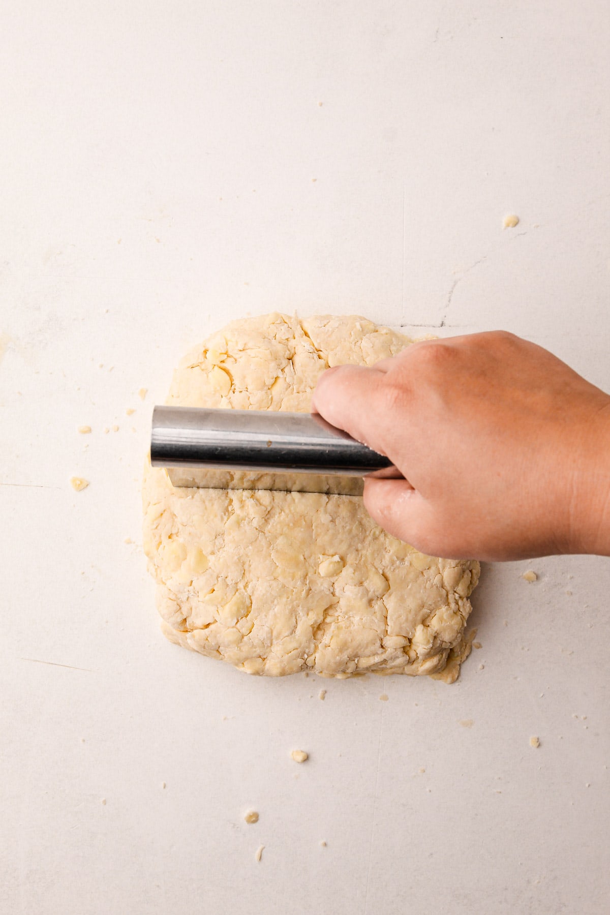 A hand using a bench scraper to cut a block of pie dough in half