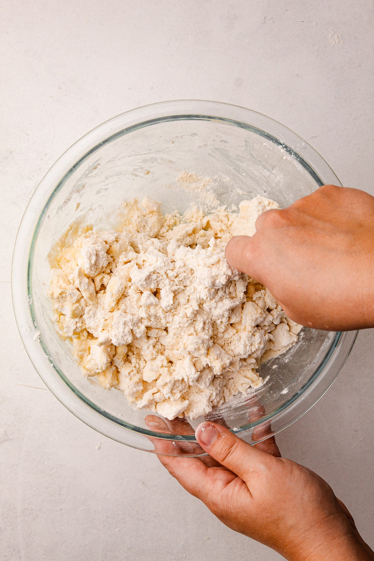 A hand pinching together butter and flour in a bowl, with a second hand holding the other side of the bowl